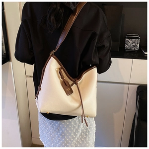 Détail du sac seau en cuir grainé crème avec bandoulières marron porté par un mannequin