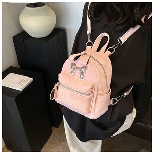 Détail d'un mini sac à dos rose avec noeud en métal argenté et texture en cuir PU poli