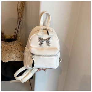 Gros plan du mini sac à dos crème avec boucle nœud argenté et texture mate élégante