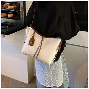 Détail du sac cabas en cuir blanc cassé avec garniture brune, pompons et pieds dorés