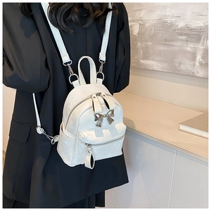 Gros plan du mini sac à dos blanc avec pendentif nœud argenté porté sur un modèle