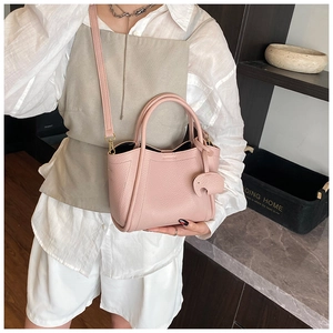Detail of pink lychee leather bucket bag with elephant charm on model in home setting