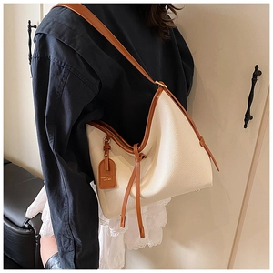 Détail d'un sac beige à grain litchi avec bordure marron et pieds de sac dorés