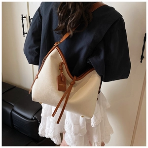 Détail du sac hobo beige avec garniture en cuir marron et pompon sur un mannequin
