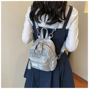 Détail d'un mini sac à dos argenté avec texture métallique et nœud sur le mannequin