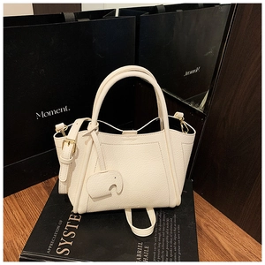 Detail of cream lychee leather bucket bag with elephant charm on designer book