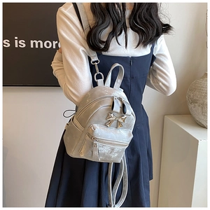 Vue détaillée du mini sac à dos argenté avec nœud doré et texture métallique chic