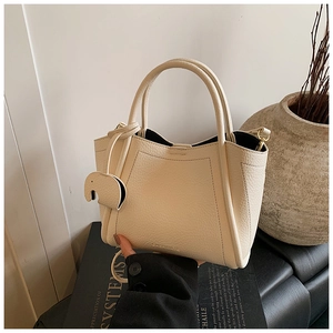 Close-up of cream pebble leather bucket bag featuring a decorative elephant charm detail
