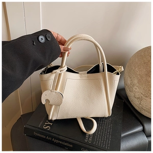 Close-up of cream pebble leather bucket bag featuring round handles and elephant charm