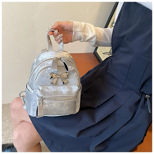Détail d'un mini sac à dos argenté avec un nœud métallique et une texture en velours