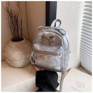 Détail d'un mini sac à dos gris clair avec texture mate et boucle nœud argentée sur bureau