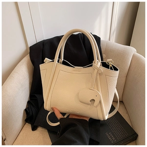 Detail of cream white lychee leather tote bag with elephant charm on beige sofa