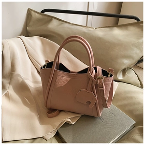 Dusty pink pebble leather bucket bag with elephant charm on beige blazer and book