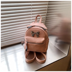 Vue latérale d'un mini sac à dos rose avec nœud métallique sur une surface élégante