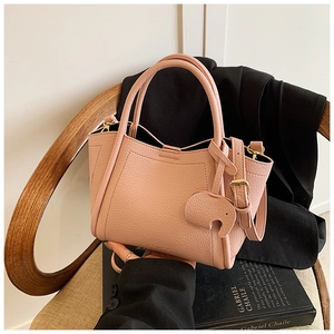 Pink lychee grain leather bucket bag with an elephant charm on a wooden chair