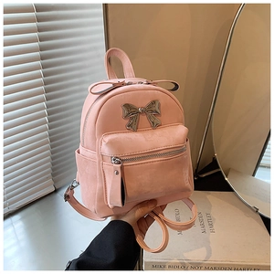 Détail d'un mini sac à dos en daim rose avec un grand nœud métallique argenté et poche avant