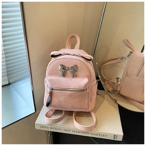 Détail du mini sac à dos rose avec nœud argenté sur des livres d'art avec reflet miroir