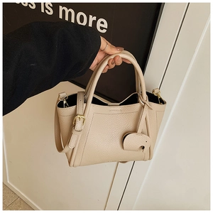 Detail of beige lychee leather bucket bag with cute elephant charm and gold hardware
