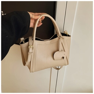Close-up of beige lychee grain leather bucket bag with cute elephant charm and gold hardware