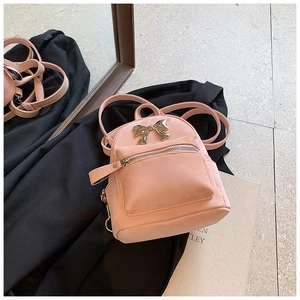 Détail d'un mini sac à dos rose en similicuir avec un nœud doré et des poches zippées