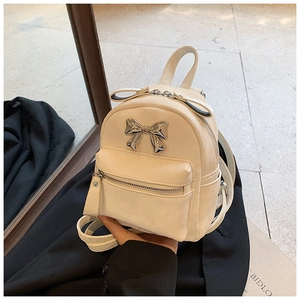 Détail d'un mini sac à dos blanc crème avec nœud en métal argenté et texture en cuir mat