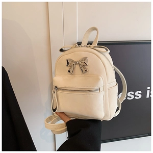 Détail d'un mini sac à dos crème avec un nœud en métal argenté et une fermeture éclair