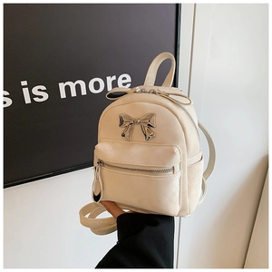 Détail d'un mini sac à dos crème avec un nœud argenté métallique et une poche zippée