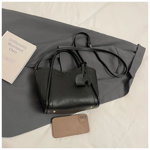 Close-up of black litchi grain leather bucket bag with cute elephant charm and strap