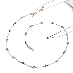 Detailed macro view of golden metal eyeglass chain with dark blue glass beads and clear loops