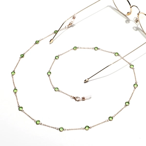 Detail view of gold metal eyewear chain with green glass gems on a white background