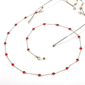 Detail of gold metal eyewear chain with red glass beads and anti-slip silicone loops
