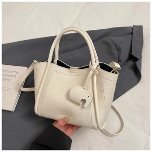 Detailed macro view of cream lychee leather tote bag featuring a cute elephant charm