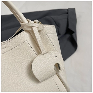Detail of off-white lychee grain leather bucket bag with a cute elephant-shaped charm