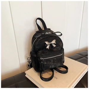 Vue détaillée d'un mini sac à dos noir avec un nœud doré sur des livres d'art