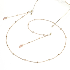Gold glasses chain with pink enamel wings and small beads on white background