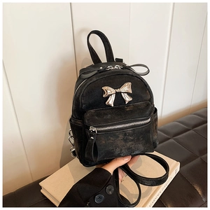 Détail d'un mini sac à dos noir avec texture vintage et un accessoire nœud en métal doré