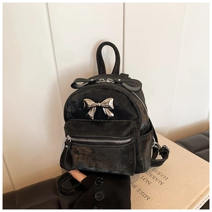 Détail d'un mini sac à dos noir avec un pendentif nœud en métal argenté et texture vintage