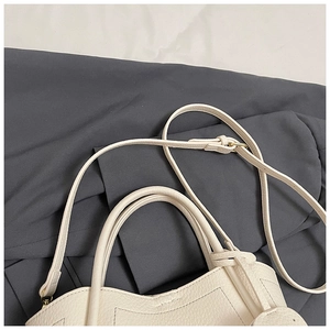 Detailed close-up of beige lychee leather bucket bag with dual handles and adjustable strap