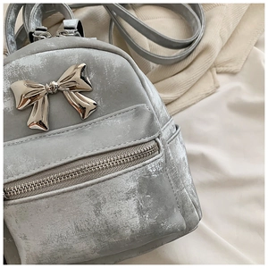 Détail d'un mini sac à dos argenté avec texture métallisée et gros nœud en métal