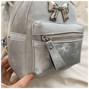 Détail du mini sac à dos gris avec texture cuir vintage et nœud métallique argenté