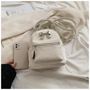 Gros plan d'un mini sac à dos beige avec nœud en métal et comparaison avec un smartphone