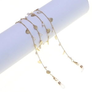 Golden eyewear chain with white pearls and metal leaf charms on a white prop display
