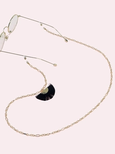 Close-up of golden eyewear chain with black fan-shaped tassels on soft pink background