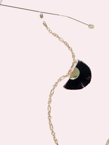 Detail of golden glasses chain with black fan tassel pendant on a pink background
