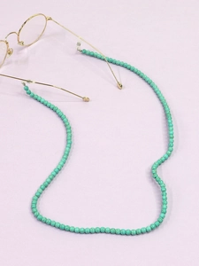 Détail de chaîne à lunettes en perles turquoise 6mm avec connecteurs dorés sur fond violet