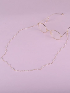 Détail d'un cordon de lunettes en perles blanches et chaîne dorée avec attaches en caoutchouc