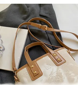 Détails de motifs floraux gaufrés et bandoulière réglable sur un sac seau crème