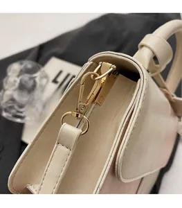 Detail shot of premium gold hook hardware on a cream leather handbag with black edges
