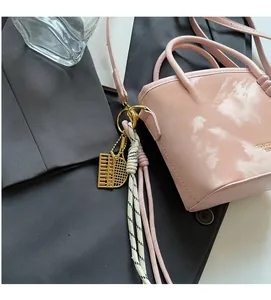 Detailaufnahme einer rosa Mini-Beuteltasche mit goldenem Abakus-Anhänger auf grauem Sakko