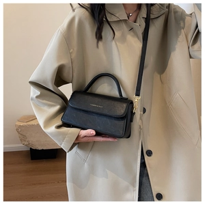 Detail of black pebbled leather handbag featuring gold logo text and top handle